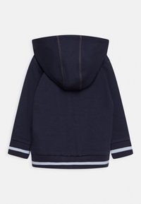 Marinblå huva sweatshirt med kontrasterande sömmar, ribbade ärmslut med ljusblå ränder och en mjuk yta. Endast bakvy.