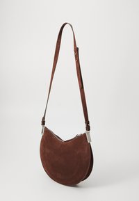 Borsa a spalla in suede marrone con forma curvilinea, tracolla regolabile e accessori in argento. Presenta una chiusura con zip e cuciture decorative.