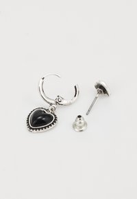 Boucle d'oreille en argent avec un pendentif en pierre noire en forme de cœur détachable. Comprend un fermoir à clou en argent. Bords texturés autour de la pierre.