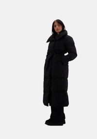 Abrigo largo negro de plumas con un cuello alto, cintura ceñida y bolsillos laterales. Textura suave con secciones acolchadas para aislamiento.