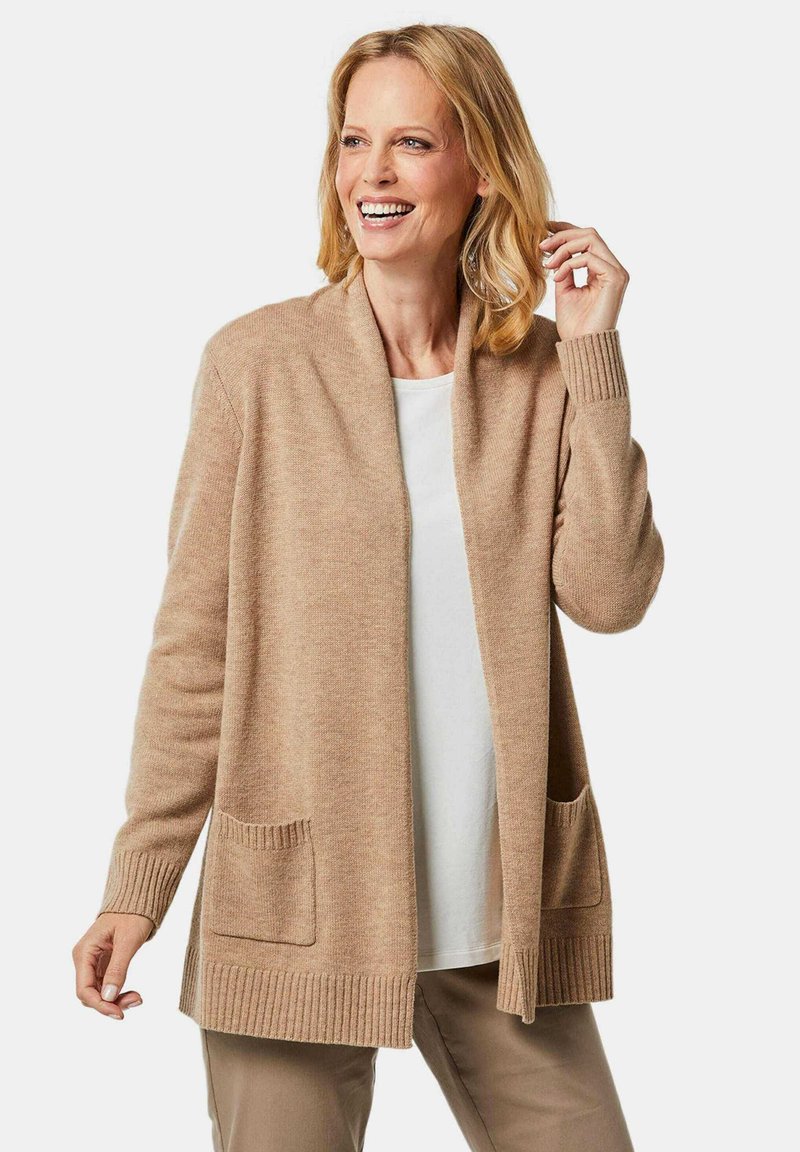 Beige gebreide cardigan met geribde manchetten en zoom, open voorkant en twee voorzakken. Zachte textuur, lichtgewicht ontwerp, geschikt voor lagen.