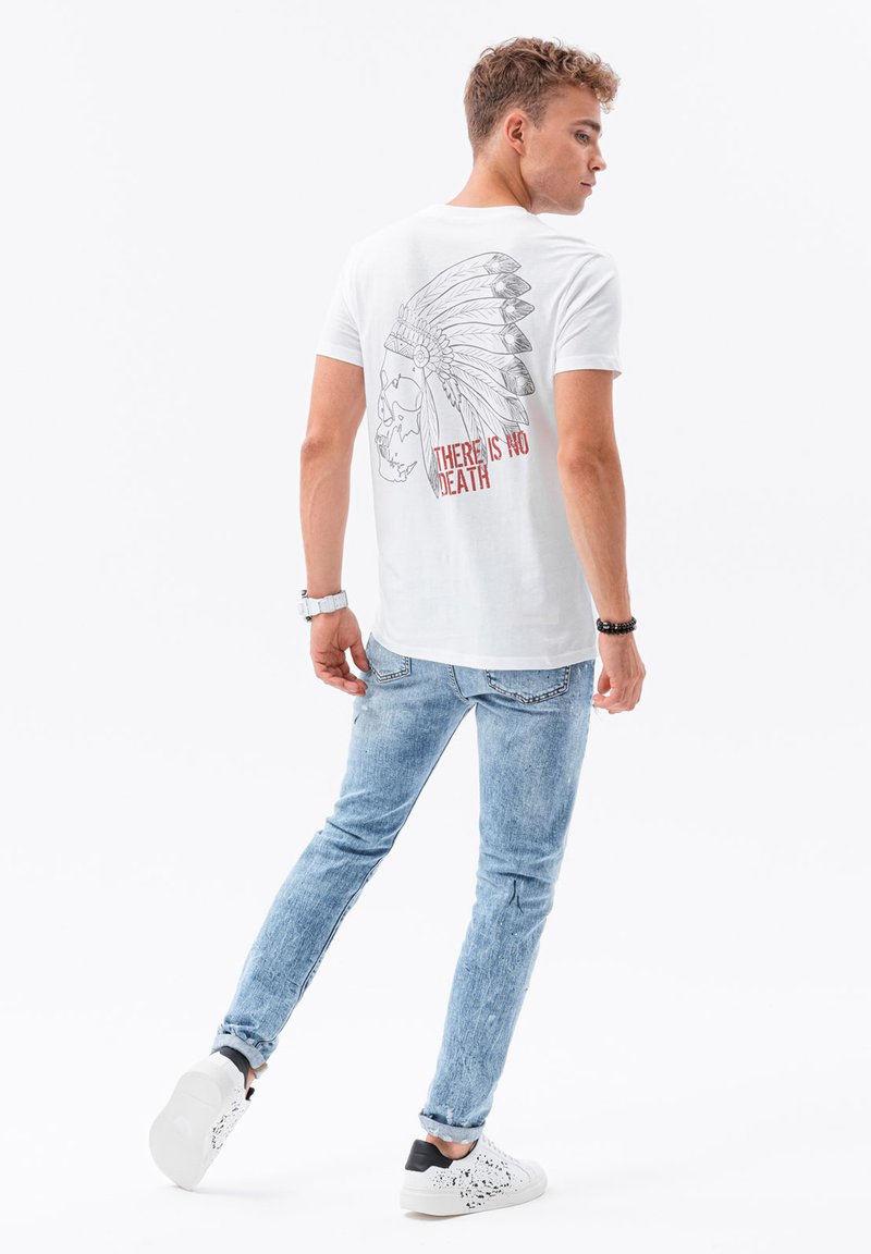Vit bomull t-shirt med en svart grafik av ett skalle och fjäderhuvudprydnad på ryggen, med röd text "DET FINNS INGEN DÖD." Bärs med blåjeans.