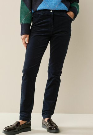 Marineblaue Cordhosen im geraden Schnitt mit mittelhoher Taille und seitlichen Taschen, kombiniert mit dunklen Lackleder-Schlupfschuhen.