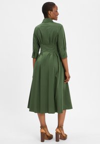 Zielona sukienka do kolan z kołnierzykiem, rękawami 3/4, plisowanym tyłem i zwiewnym dołem. Noszona z brązowymi sandałami na słupku.