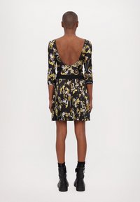 Black dress with a deep v-back, three-quarter sleeves, and a pleated skirt featuring yellow and white floral patterns. Worn with black boots.
