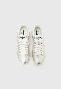 Ζευγάρι ασημένια μεταλλικά χαμηλά αθλητικά παπούτσια με λευκά κορδόνια και ενθέματα με λογότυπο, σε θέα από πάνω σε απλό λευκό φόντο.