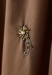 Petit motif décoratif en forme d’éclat solaire avec perles dorées et argentées sur tissu marron texturé.