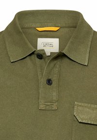 Olivengrøn poloshirt med ribbet krave, to sorte knapper, lommelåg og et Camel Active-mærke inde i kraven.