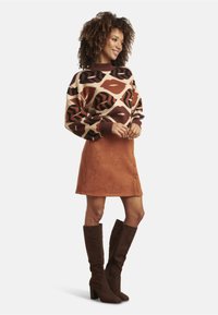 Knit sweater with abstract brown and cream pattern, paired with a rust-colored suede A-line skirt featuring front buttons and brown suede knee-high boots.
