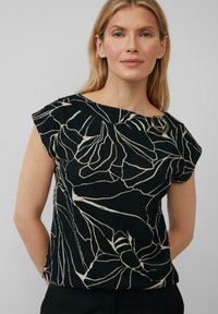 Zwart kortemouwen top met een wit bloemenpatroon, textuurstof en een ronde accent bij de schouder. Ontspannen pasvorm.