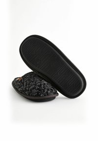 Black and white textured slippers with a soft knitted upper, contrasting black rubber sole, and a small brown label on the side.