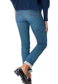 Jeans en denim bleu à coupe slim, avec un revers à la cheville et des coutures visibles sur les poches arrière. Assortis avec des mocassins noirs.