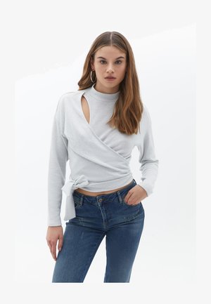 Jasnoszara bluzka o kroju z paskiem z długimi rękawami, wysokim dekoltem i wycięciem. W połączeniu z ciemnoniebieskimi dżinsami o klasycznym kroju i lekko postrzępionych.