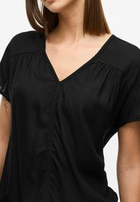 Blusa nera a V con maniche corte, caratterizzata da tessuto arricciato e bordino in pizzo lungo il collo e la patta anteriore, realizzata in un materiale liscio.