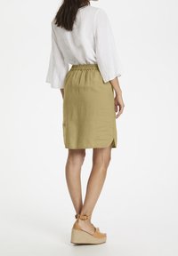 Jupe longueur genou de couleur vert olive avec taille élastique, fente latérale et finition texturée, accompagnée de compensées espadrilles couleur tan.