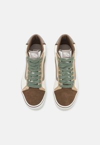 Zapatillas altas que presentan una combinación de ante marrón y beige, cordones verdes y una suela de goma blanca. Marcado en la lengüeta.