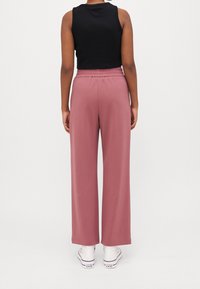 Světle růžové široké kalhoty s elastickým pasem, kombinované s přiléhavým černým topem bez rukávů, obuté s bílými teniskami.