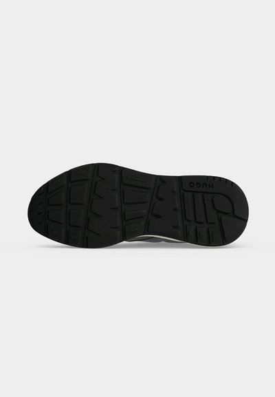 Semelle en caoutchouc noire d'une chaussure avec des rainures à motifs et le nom de la marque "HUGO" embossé près du talon.