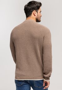 Beżowy sweter dzianinowy z teksturowanym wzorem, ze ściągaczami przy mankietach i u dołu, o luźnym kroju i okrągłym dekolcie.