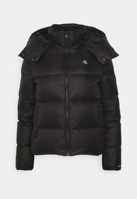 Veste matelassée noire avec col montant, fermeture éclair à l'avant, deux poches zippées, capuche amovible et petit logo blanc "cK" sur la poitrine.