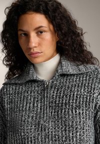 Pletený svetřík v černé a bílé barvě se stojáčkem na zip, zdobený texturovaným vzorem a volným střihem.