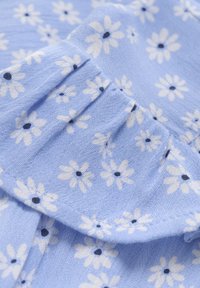 Blått tyg med ett blommönster av vita blommor med mörka mitten, med subtil textur och insamlad detalj längs kanten.