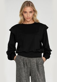 Czarny sweter z długim rękawem, okrągłym dekoltem i falbankami na ramionach, w połączeniu z teksturowanymi, szarymi spódnicami plisowanymi. Gładka faktura materiału.