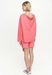 Przesadnie duża koralowa bluza z kapturem z marszczonym dekoltem, w zestawie z dopasowanymi szortami. Materiał wydaje się miękki; posiada subtelny znaczek logo z tyłu.