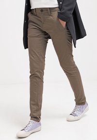 Slim-fit khaki bukser med sidelommer, en knaplukning og en glat overflade, parret med sølvfarvede sneakers med en skinnende overflade.
