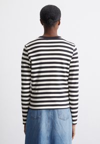 Langärmliges Oberteil mit schwarzem und weißem Streifenmuster und rundem Ausschnitt, kombiniert mit einem Jeansrock, von hinten betrachtet.