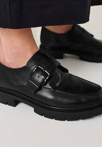 Must musta nahkkingad sileda viimistlusega, millel on silmapaistev pandla rihm ja paks kummitald, millel on ristkülikukujuline mustr.