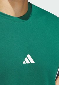 Zelené sportovní tričko s texturovaným povrchem, na levé části hrudi s bílým logem v trojúhelníkovém designu.