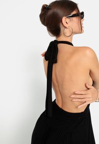 Melnā halter kleita ar atvērtu muguru, ar kakla saitēm un savilktu jostasvietu. Gluda auduma un plūstošs svārks.