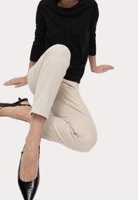 Maglione nero con scollo ampio, pantaloni beige a gamba dritta e ballerine nere a punta con silhouette elegante. Schema di colori neutro, minimalismo nei dettagli.