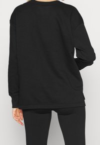 Svart sweatshirt med rundad halsringning, långa ärmar och en avslappnad passform, tillverkad av mjukt tyg med en slät textur.