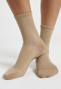 Calcetines de tobillo de canalé beige con un acabado metálico texturizado brillante, que cuentan con un puño enrollado y una zona de punta suave.
