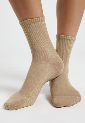 Beige ribbed ankle socks with a textured metallic shimmer finish, featuring a rolled cuff and smooth toe area.