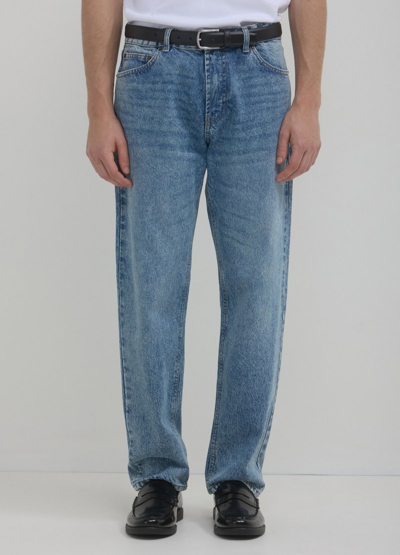 Jean en denim bleu clair à coupe relaxée, avec des passants de ceinture, des poches avant et un effet délavé. Accompagnés de chaussures noires.