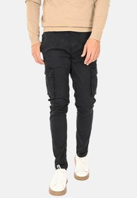 Pantaloni cargo neri con una vestibilità slim, dotati di tasche laterali e una texture morbida, abbinati a sneakers bianche e a un maglione beige.