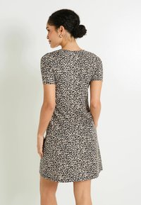 Robe à manches courtes avec un imprimé léopard, présentant un fond beige avec des taches noires, fabriquée à partir d'un tissu lisse et texturé.