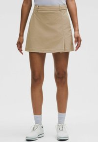 Beige golfrok met een vlakke voorkant, zijsplit en riemlussen. Gemaakt van lichte, ademende stof met een soepele textuur.