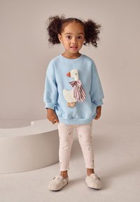 Hellblaues Sweatshirt mit einer Enten-Applikation und gestreiftem Schleifchen, kombiniert mit rosa Leggings mit kleinen Blumenmustern und flauschigen Hausschuhen.