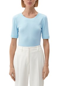 Ljusblå kortärmad topp med rund halsringning, figursydd design och slät textur, tillsammans med högmidjade vita byxor.