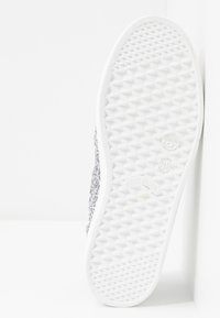 Vit sneakersula med geometriskt mönster, storlek 38, "Made in Italy" märkning och delvis synlig silverglitter på ovandelen.