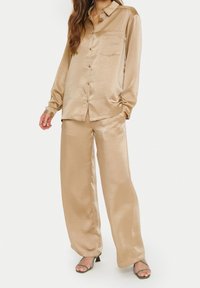 Beige Satinhemd mit langen Ärmeln und Knöpfen, kombiniert mit passenden, weit geschnittenen Hosen. Verfügt über eine Brusttasche, glatte Textur und taillierten Schnitt.