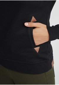 Fekete pulóver elején háromszög alakú barna bőr díszítéssel és bordázott mandzsettákkal. Puha, sima tapintású anyag.