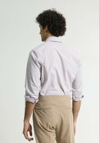 Camisa a cuadros de color púrpura claro con las mangas remangadas, combinada con pantalones beige que cuentan con dos bolsillos traseros y un ajuste suave y entallado.