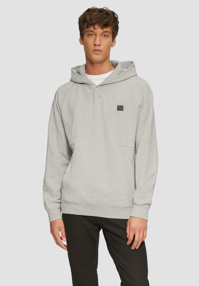 Sudadera gris con un bolsillo frontal, mangas raglán y cierre de botones a presión. Presenta un parche con logo en el lado izquierdo del pecho. La tela parece suave.