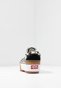 Baskets Vans à damier noir et blanc vues de derrière, semelle en gomme et logo rouge Vans “Off the Wall” sur le talon blanc.