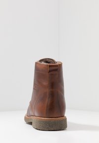 Barna bőr bokacsizma texturált talppal. Puha szőrme bélése van, és egy logó van a oldalán. Klasszikus, lekerekített design.